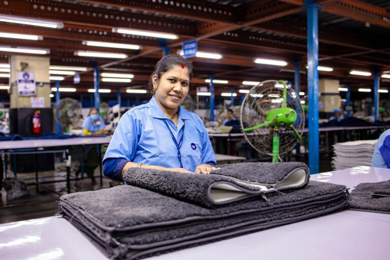 A smiling female textile worker in a busy factory setting folding fabric.