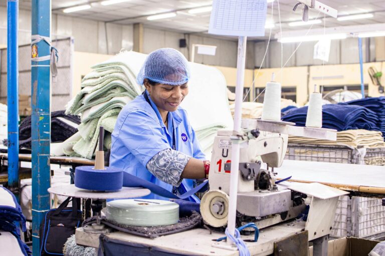 Female worker operates sewing machine in bright textile factory.