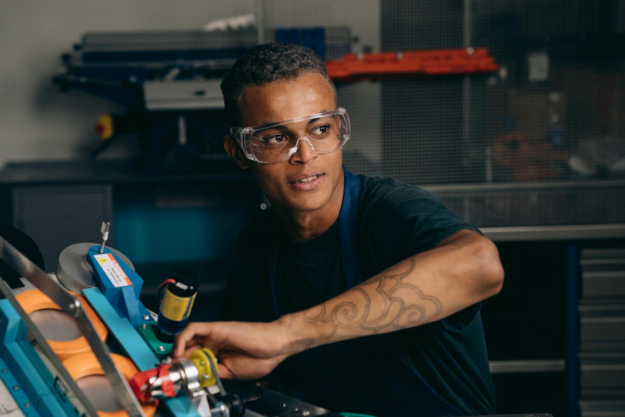 Young engineer working with machinery in a manufacturing setting, wearing safety glasses and focusing intently.